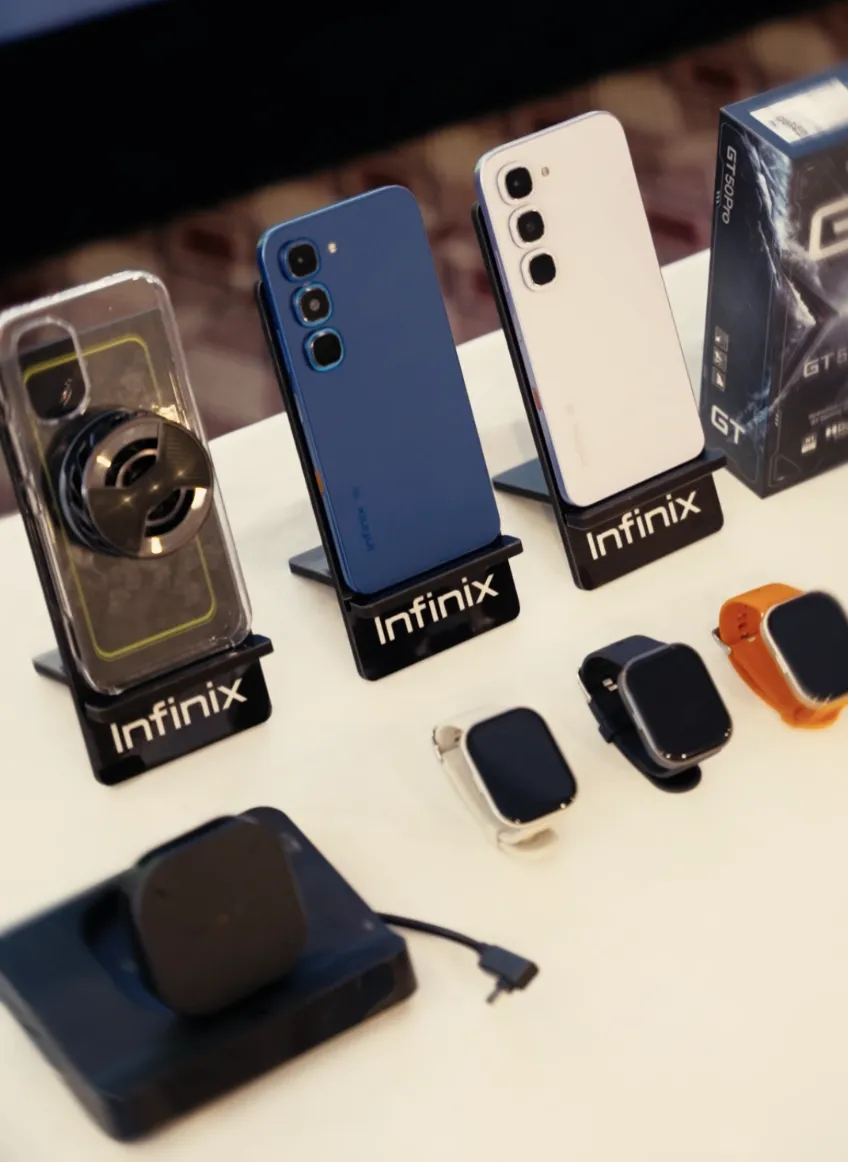 Infinix phones on display stands with a magnetic cooler, Infinix smartwatches and a retail box at the GT 50 Pro launch event