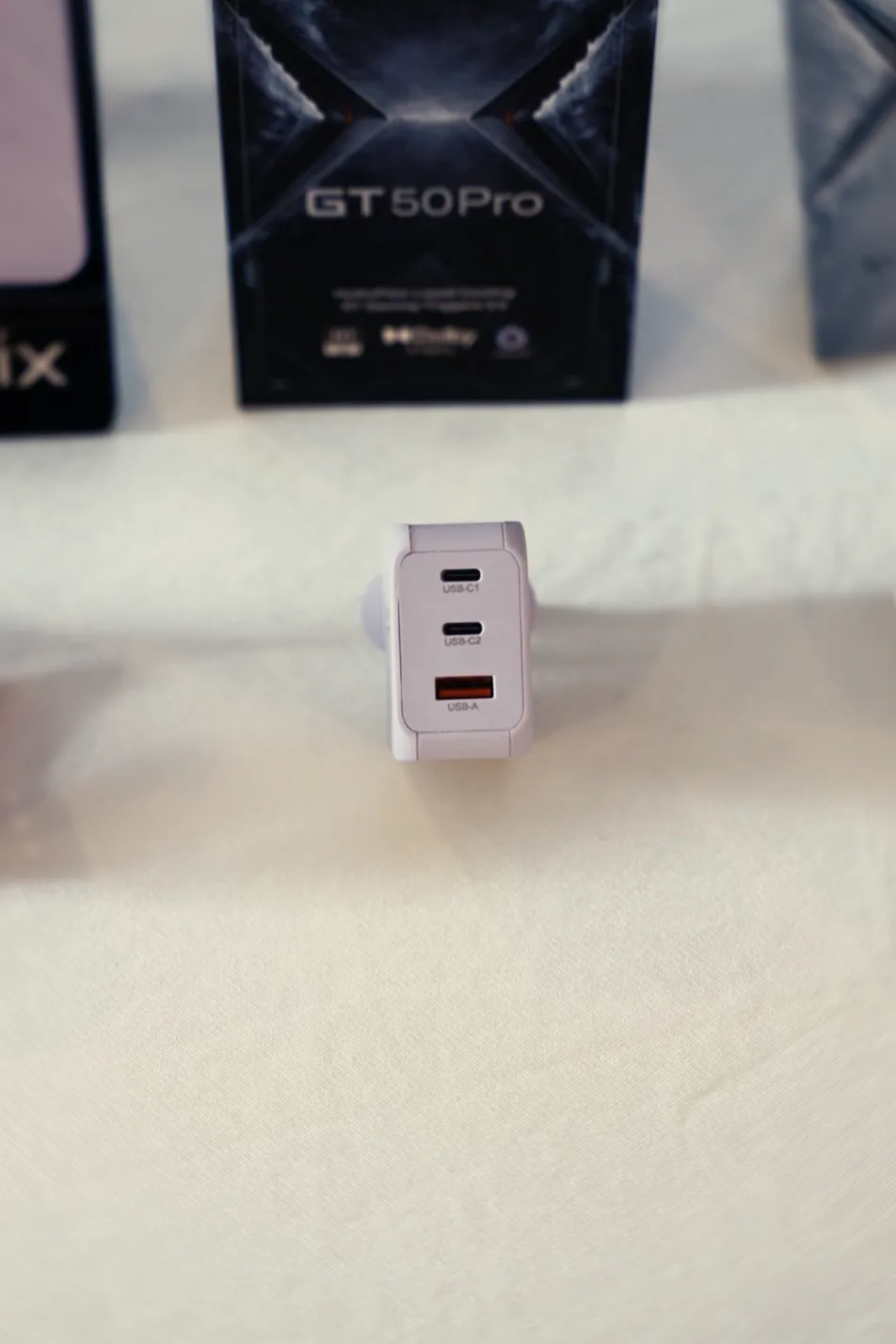 An Infinix GaN charger in front of the GT 50 Pro retail box